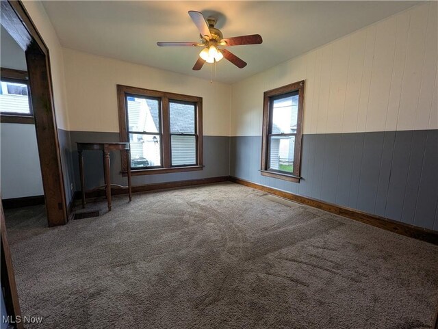 unfurnished living room with ceiling fan, carpet, baseboards, and wooden walls