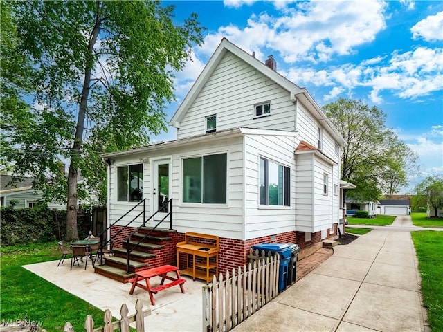 bungalow-style home with entry steps, a chimney, a patio, and a front lawn