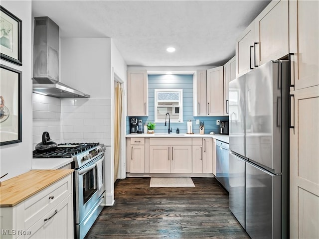 kitchen with stainless steel appliances, wall chimney range hood, a sink, tasteful backsplash, and dark wood-style floors