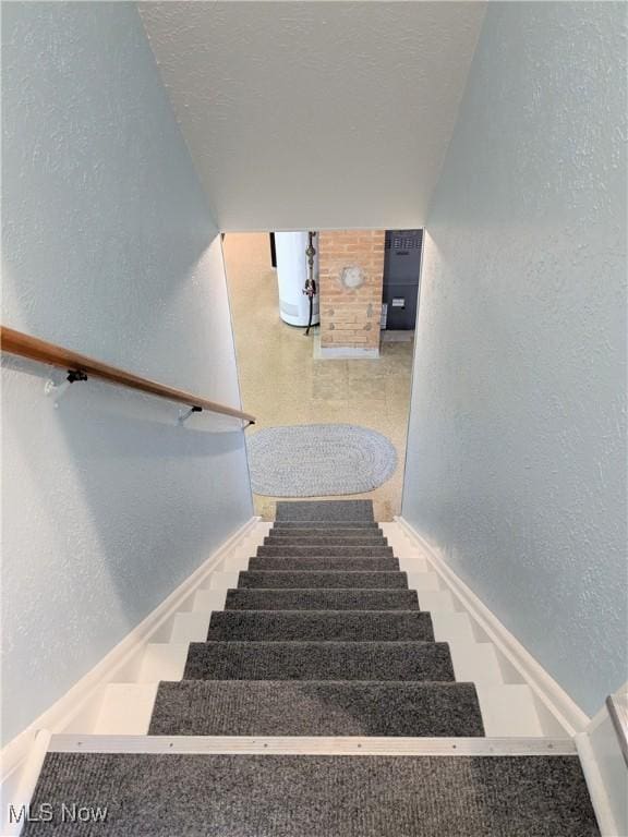 staircase featuring a textured wall, water heater, and baseboards