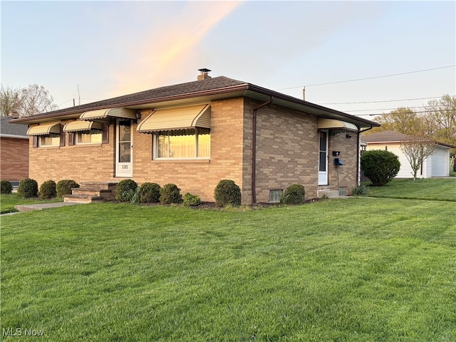 view of side of home featuring a chimney, brick siding, and a yard