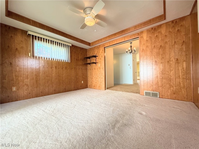 carpeted spare room featuring wooden walls, a chandelier, and ceiling fan