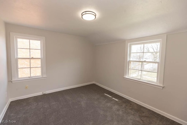 unfurnished room featuring dark carpet, baseboards, and lofted ceiling