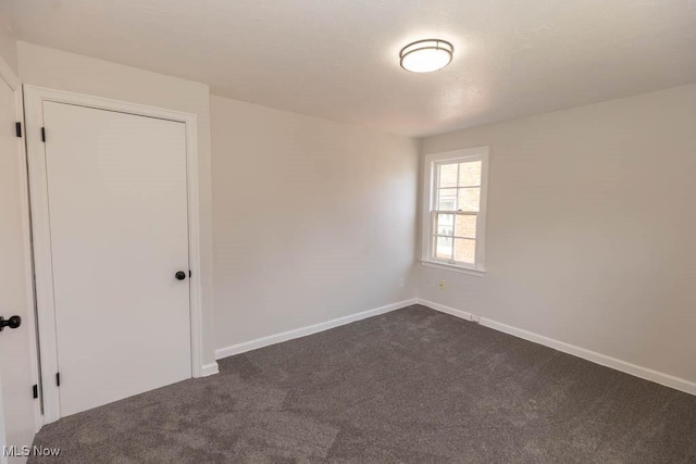unfurnished room featuring dark colored carpet and baseboards