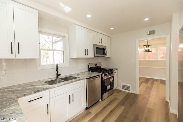 kitchen with appliances with stainless steel finishes, a sink, light stone countertops, white cabinetry, and recessed lighting