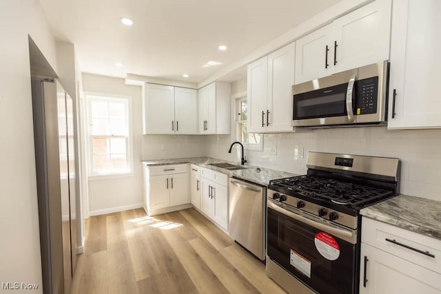 kitchen with stainless steel appliances, a sink, white cabinets, light stone counters, and recessed lighting