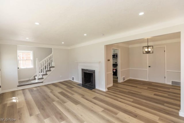 unfurnished living room featuring stairway, a chandelier, light wood-style floors, recessed lighting, and a fireplace with flush hearth