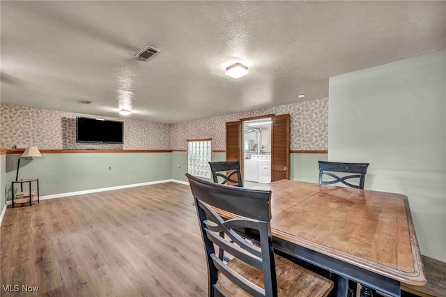 dining area with wallpapered walls, washing machine and dryer, wood finished floors, a textured ceiling, and baseboards