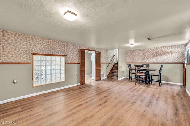 dining room with wallpapered walls, a textured ceiling, stairs, wood finished floors, and baseboards