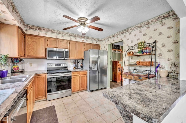 kitchen featuring appliances with stainless steel finishes, wallpapered walls, a ceiling fan, a textured ceiling, and a peninsula