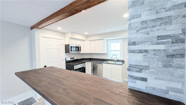 kitchen with appliances with stainless steel finishes, a sink, beam ceiling, dark countertops, and white cabinets
