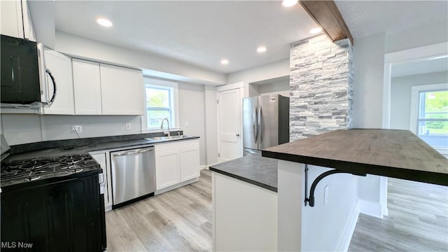 kitchen featuring stainless steel appliances, dark countertops, a sink, light wood-type flooring, and white cabinetry