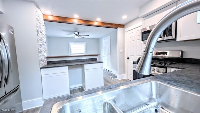kitchen featuring stainless steel appliances, dark countertops, white cabinets, wood finished floors, and beam ceiling