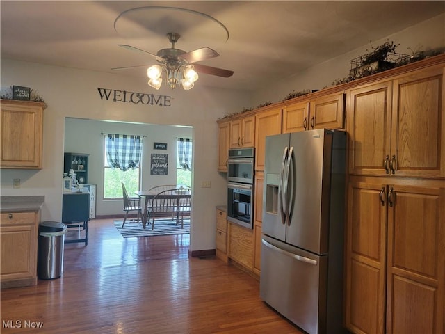 kitchen featuring stainless steel appliances, a ceiling fan, wood finished floors, brown cabinetry, and dark countertops