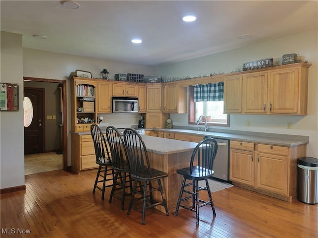 kitchen with appliances with stainless steel finishes, light wood-style flooring, a kitchen bar, a center island, and light countertops