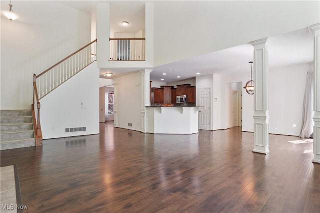 unfurnished living room featuring ornate columns, dark wood-style flooring, stairway, a towering ceiling, and recessed lighting