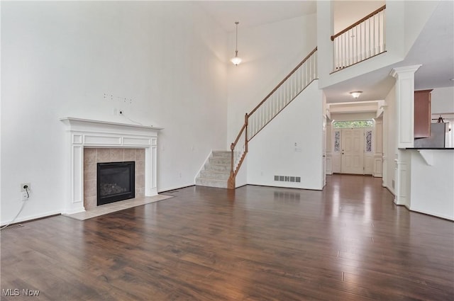 unfurnished living room featuring wood finished floors, a fireplace, stairway, and a high ceiling