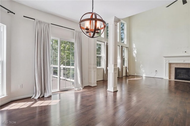 unfurnished living room featuring ornate columns, wood finished floors, a chandelier, and a tiled fireplace