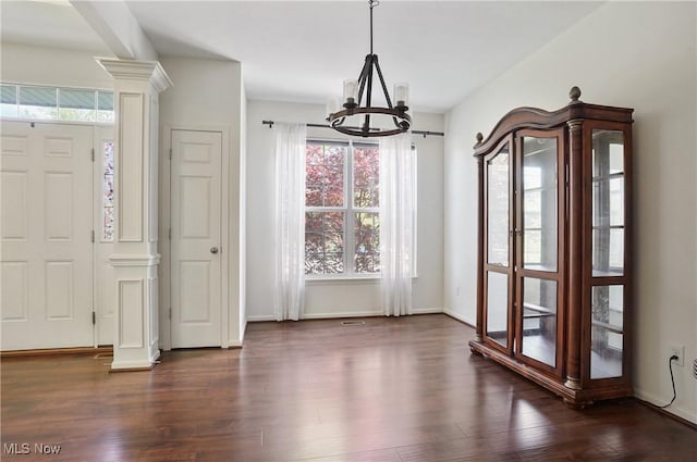 unfurnished dining area featuring a chandelier, dark wood finished floors, ornate columns, and baseboards