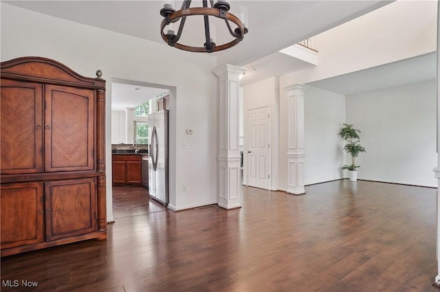 unfurnished room with a chandelier, decorative columns, and dark wood finished floors