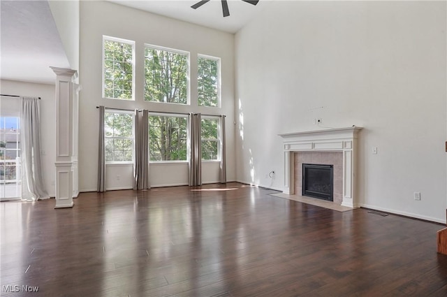 unfurnished living room featuring a towering ceiling, ceiling fan, plenty of natural light, a tile fireplace, and ornate columns