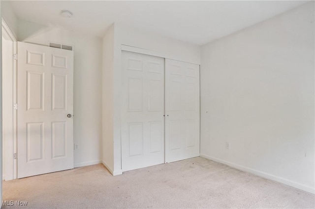 unfurnished bedroom with light colored carpet, a closet, and baseboards