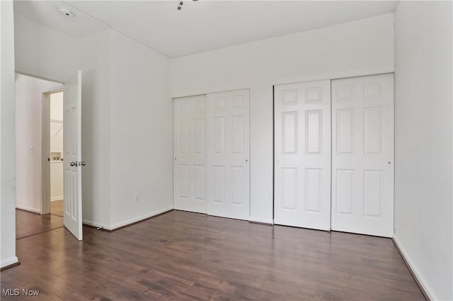 unfurnished bedroom featuring multiple closets, wood finished floors, and baseboards
