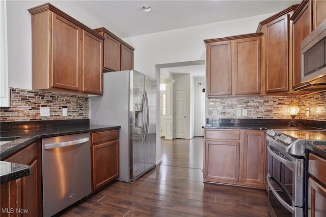 kitchen featuring stainless steel appliances, backsplash, dark stone countertops, dark wood-style flooring, and brown cabinetry