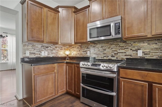 kitchen featuring appliances with stainless steel finishes, dark wood-type flooring, backsplash, brown cabinetry, and dark stone counters
