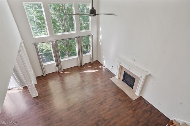 unfurnished living room featuring a premium fireplace, a ceiling fan, wood finished floors, and a towering ceiling