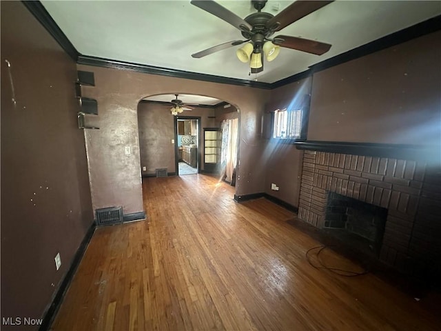 unfurnished living room featuring arched walkways, ceiling fan, a fireplace, baseboards, and wood finished floors