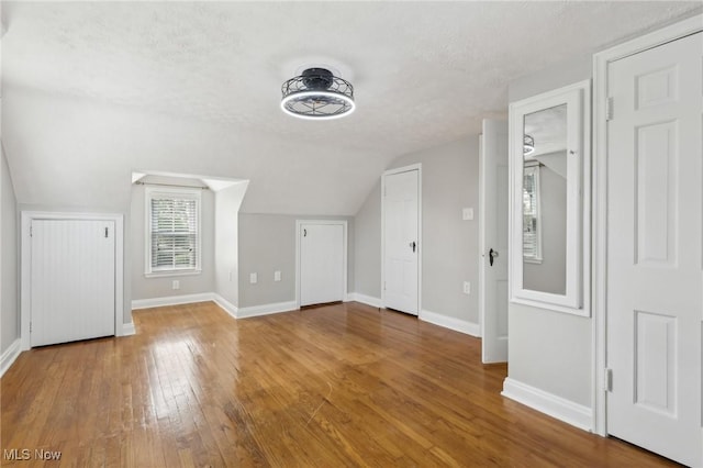 additional living space featuring hardwood / wood-style flooring, vaulted ceiling, baseboards, and a textured ceiling