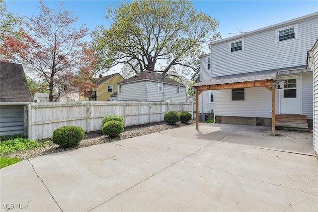 rear view of property featuring fence, a patio area, a shingled roof, and central air condition unit