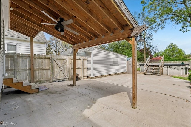 view of patio / terrace with a storage unit, a ceiling fan, an outbuilding, fence, and a gate