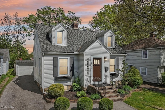 cape cod home featuring an outbuilding, a chimney, a shingled roof, and a garage