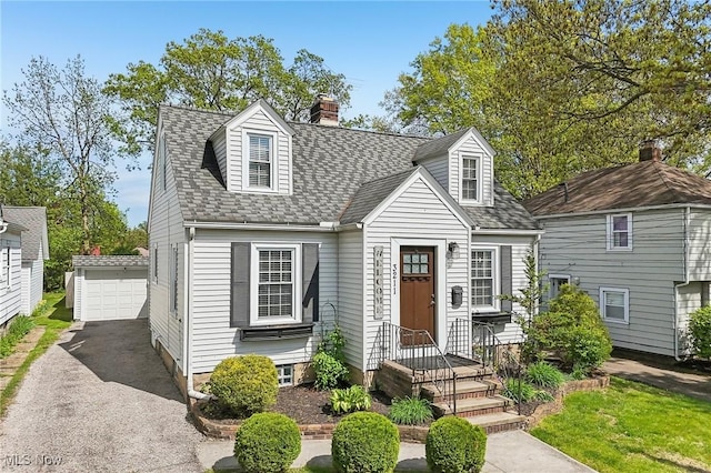 new england style home with roof with shingles, an outdoor structure, a chimney, and a detached garage