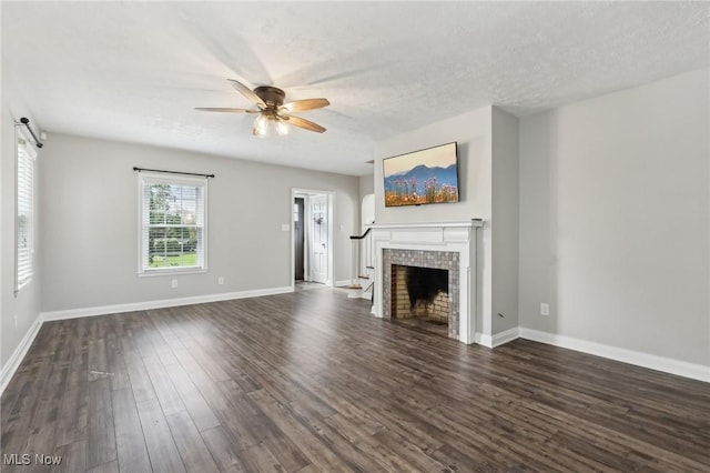unfurnished living room with ceiling fan, dark wood-type flooring, a tiled fireplace, baseboards, and a textured ceiling