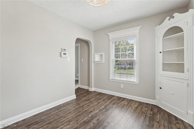 unfurnished room featuring dark wood finished floors, arched walkways, and baseboards