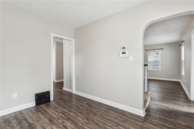 empty room with arched walkways, dark wood-type flooring, and baseboards