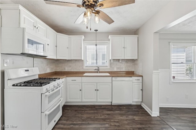 kitchen featuring white appliances, a sink, ceiling fan, white cabinets, and a wainscoted wall