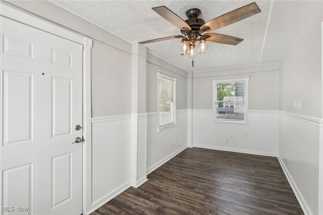 spare room with a textured ceiling, dark wood-type flooring, a ceiling fan, and a wainscoted wall