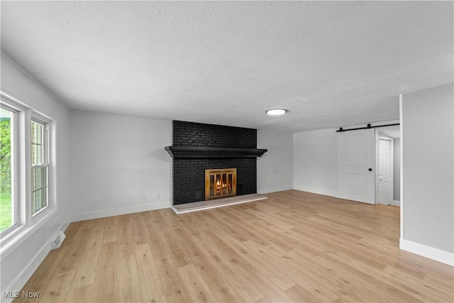 2394 Reimer Rd, Wadsworth, OH 44281 - unfurnished living room with a textured ceiling, a fireplace, light wood-style floors, a barn door, and baseboards