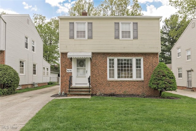 colonial-style house with brick siding, a front yard, a chimney, and entry steps