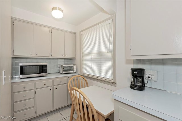 kitchen with stainless steel microwave, light countertops, decorative backsplash, and light tile patterned flooring