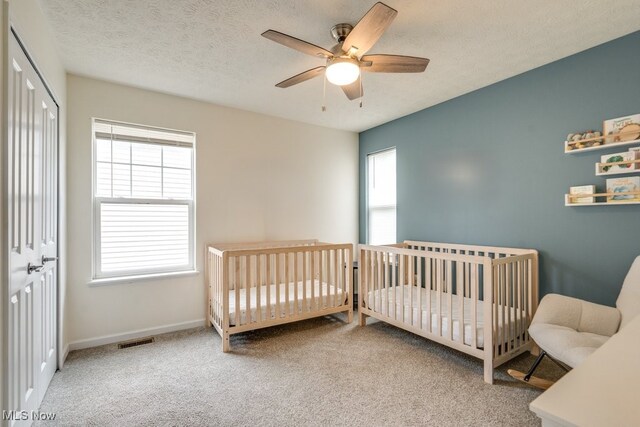 3585 Gerome Ct, Cleveland, OH 44105 - carpeted bedroom with multiple windows, a nursery area, ceiling fan, a closet, and a textured ceiling