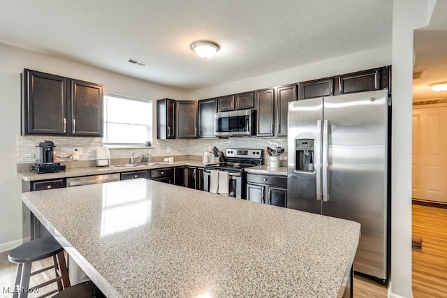 3585 Gerome Ct, Cleveland, OH 44105 - kitchen featuring stainless steel appliances, dark brown cabinetry, a breakfast bar, backsplash, and light wood-type flooring