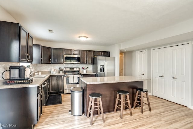 3585 Gerome Ct, Cleveland, OH 44105 - kitchen with stainless steel appliances, light wood-style flooring, a breakfast bar, a center island, and backsplash