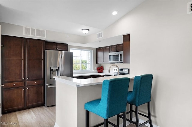 kitchen featuring stainless steel appliances, a breakfast bar area, a peninsula, light wood-style flooring, and light countertops