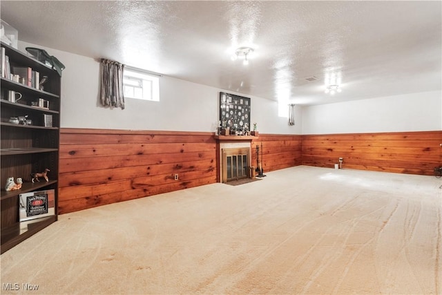 basement with wooden walls, a wainscoted wall, carpet floors, a fireplace with flush hearth, and a textured ceiling