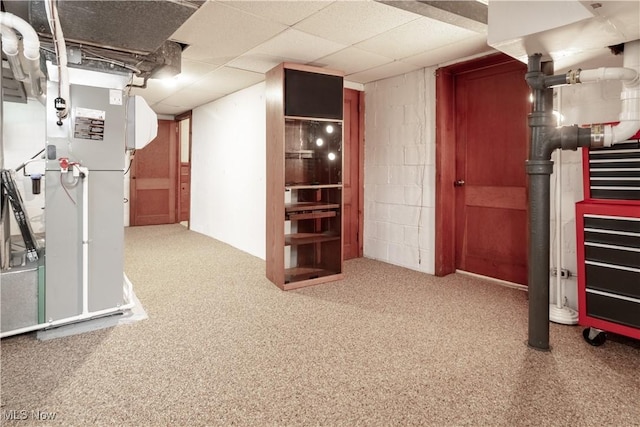 finished basement with concrete block wall, heating unit, carpet floors, and a drop ceiling